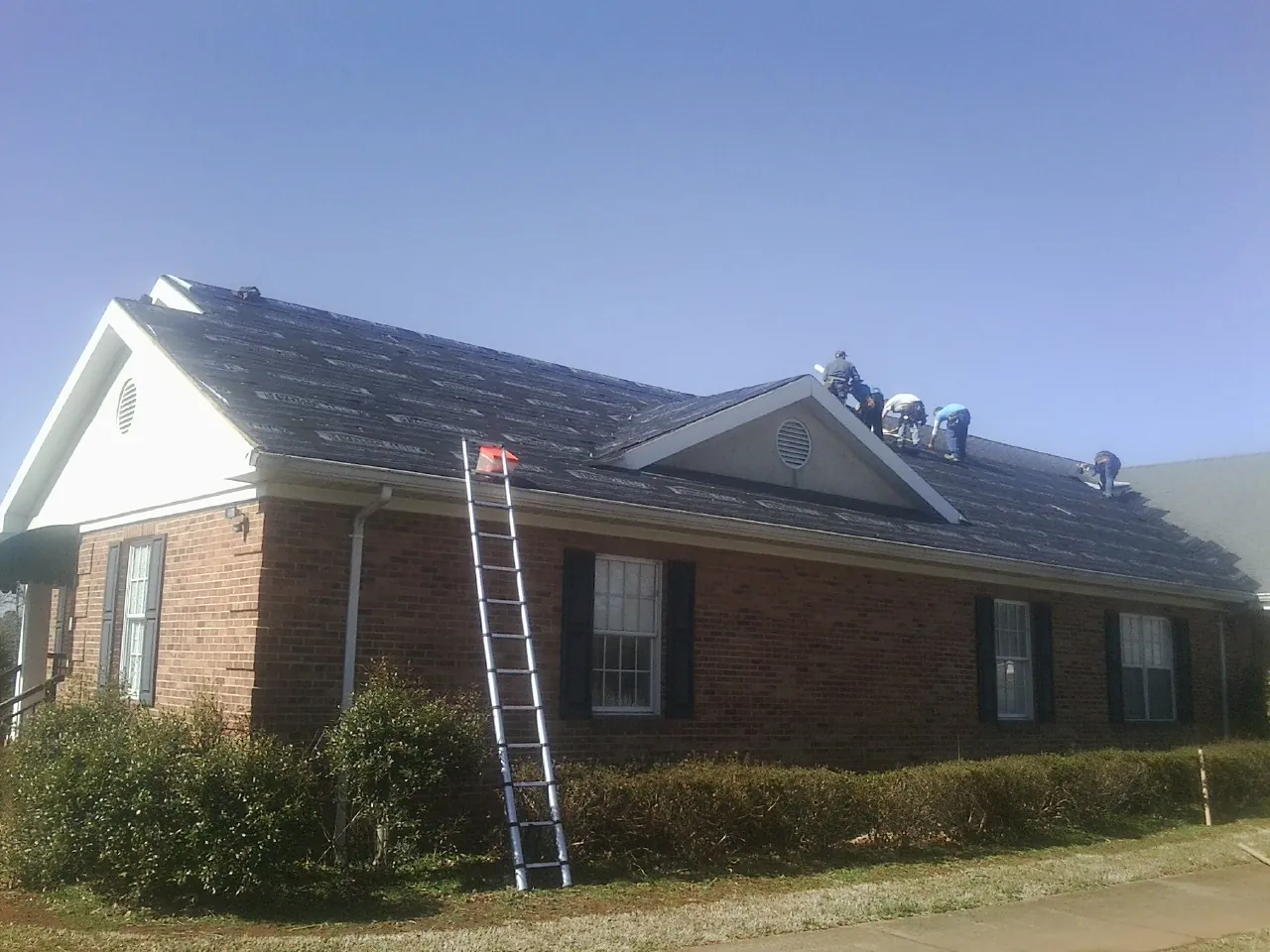 Crew tearing shingles off a brick ranch roof with a ladder set — Emergency Roof Repair work by our crew in Seal Beach