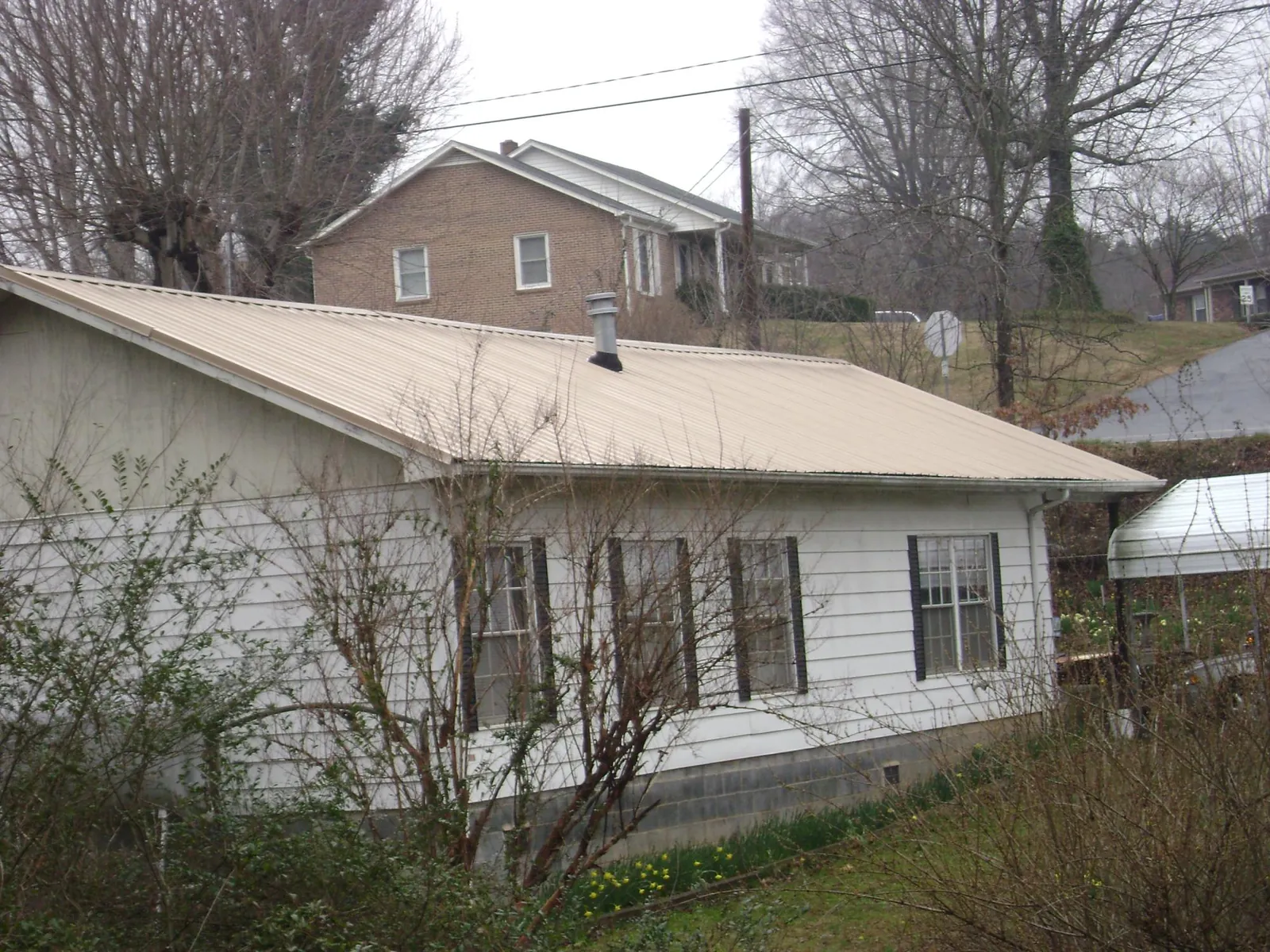 Tan metal roof on a white sided house set into a hillside — Commercial Roofing by Roofing Brothers in Seal Beach
